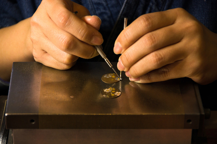 A Japanese artisan delicately inlays fine gold patterns onto a circular metal plate using traditional tools in the intricate process of Kyo-zogan (Kyoto metal inlay craftsmanship).